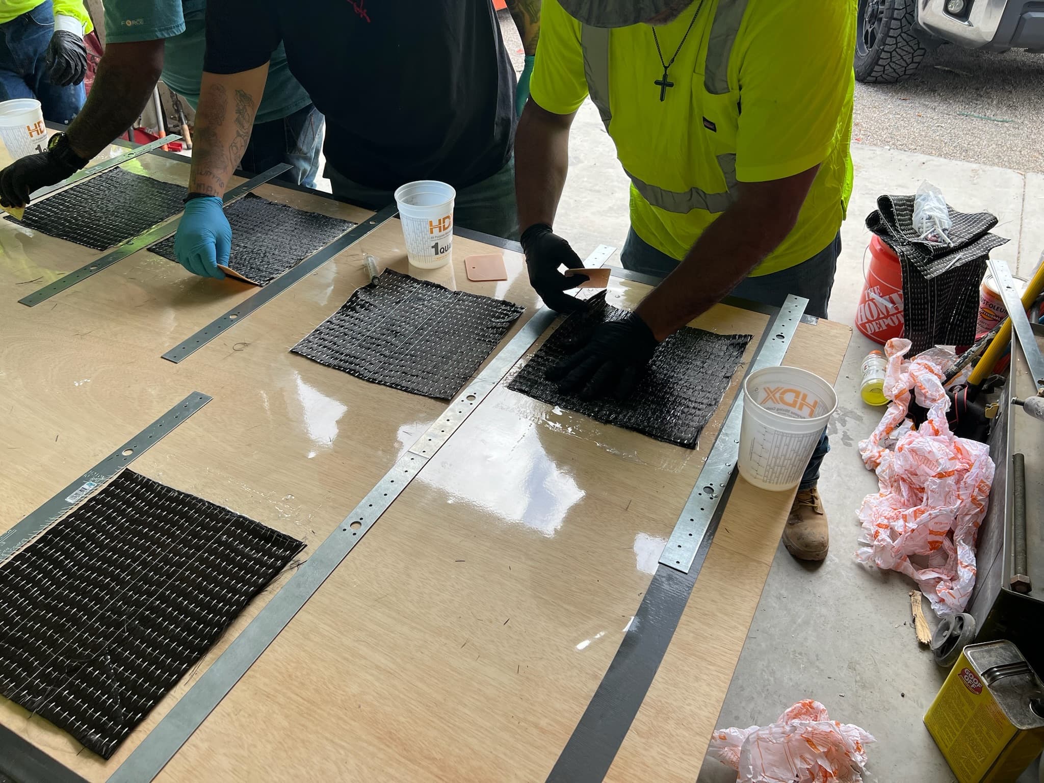 Trainees consolidating carbon fiber sample laminates with squeegees