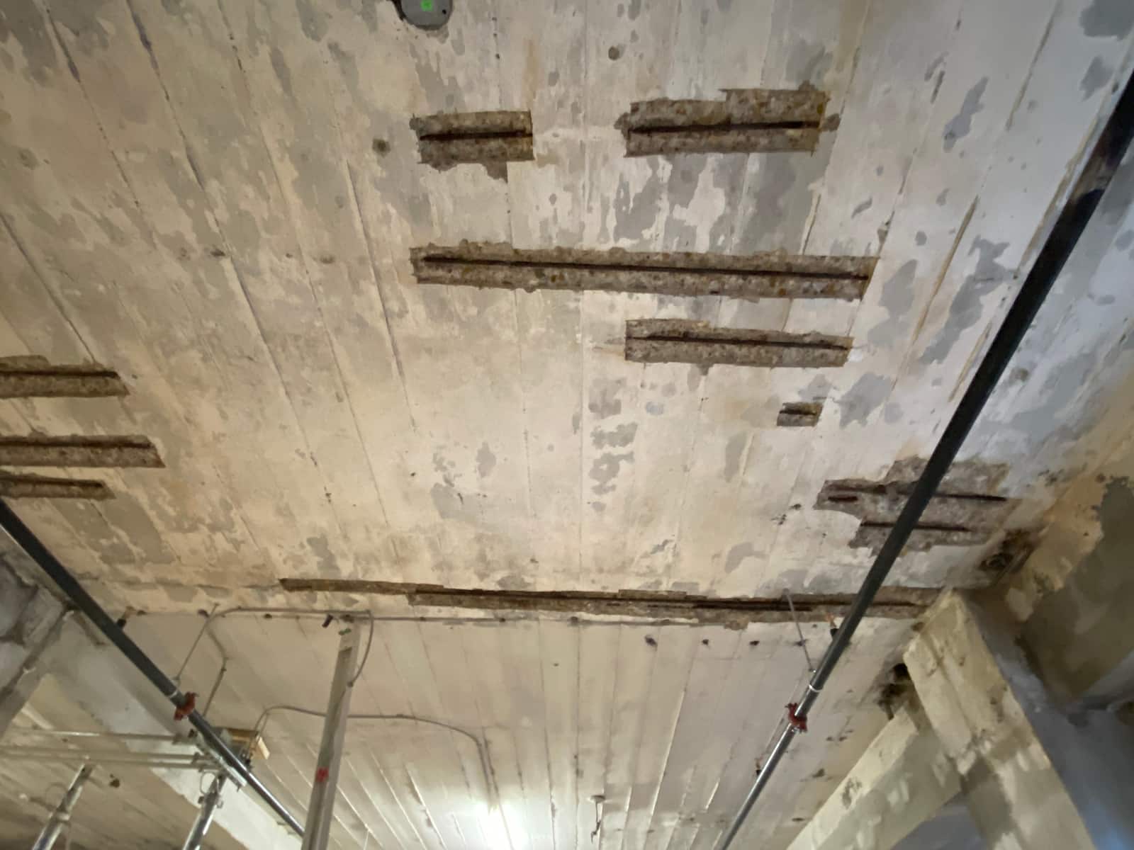 Slab soffit with rectangular strips of concrete removed to expose rebar.