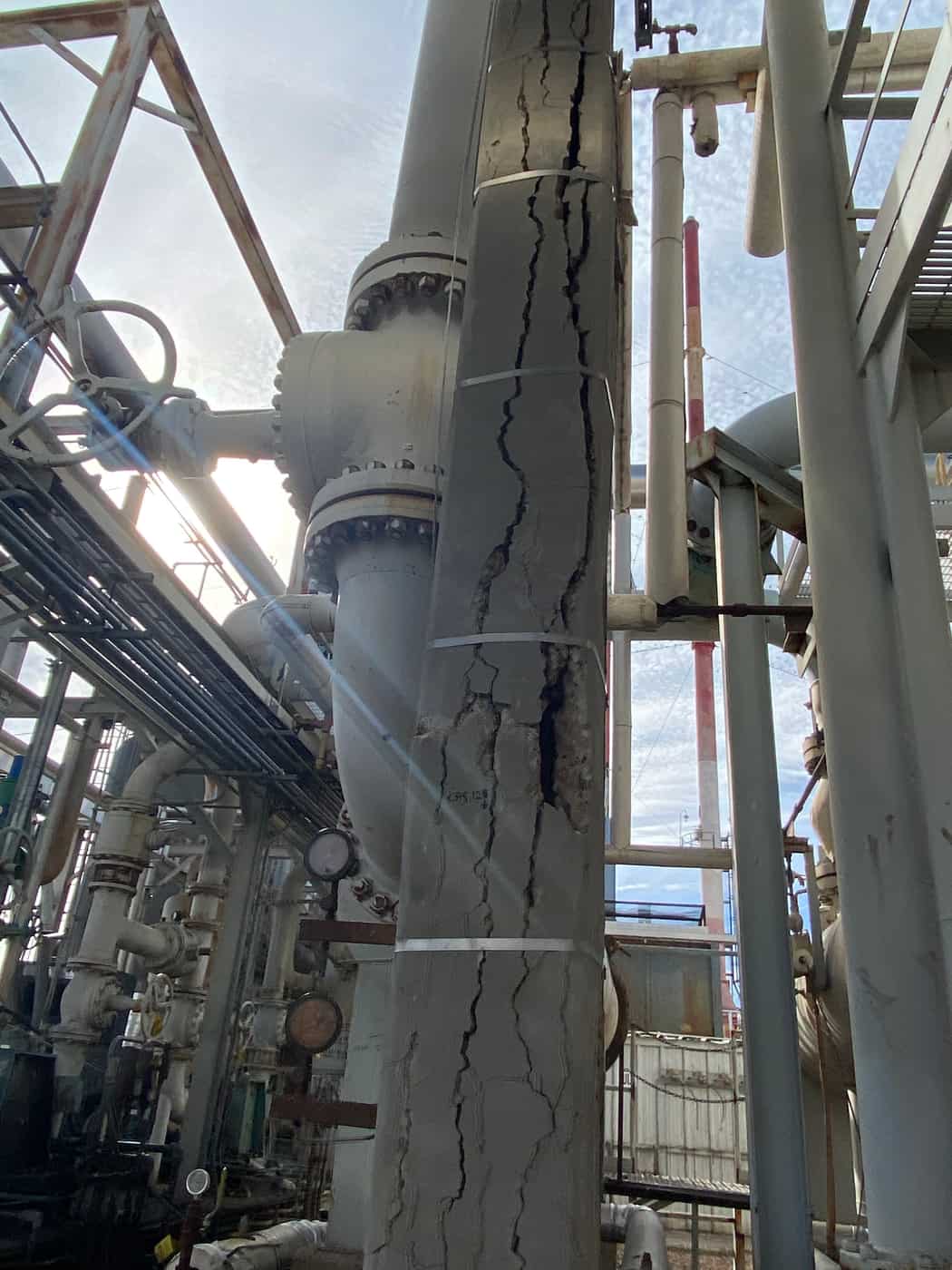 Tall concrete column with long vertical cracks among process piping.