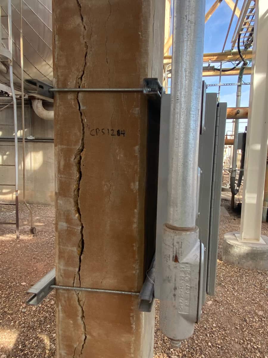 Close view of a concrete column with vertical cracks and a steel clamp bracket.