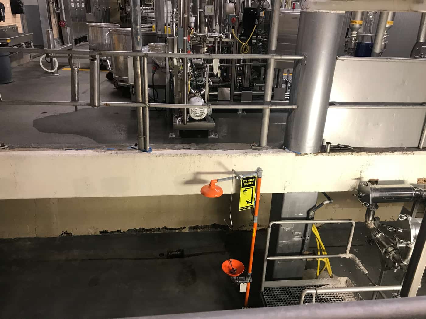 Concrete platform curb with deteriorated base below stainless process equipment.