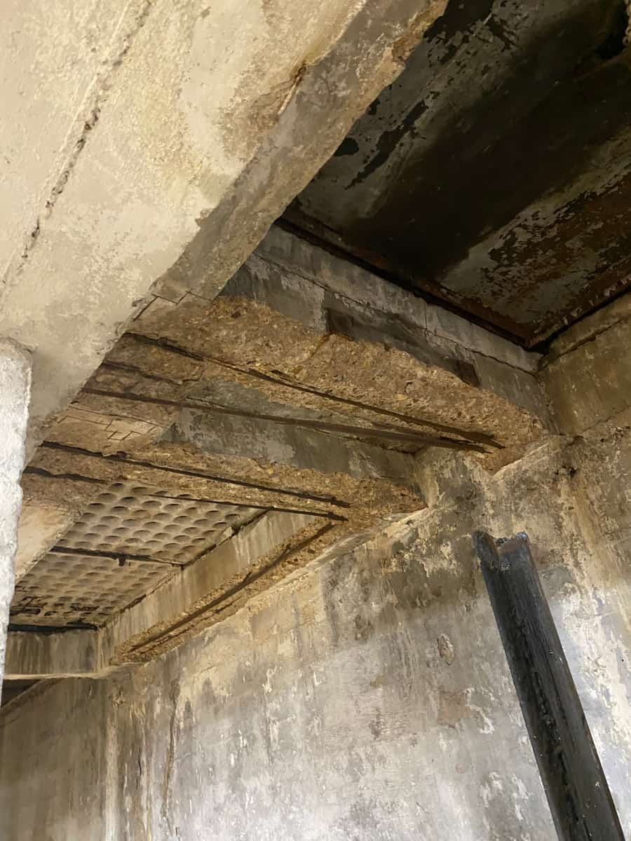 Slab underside with deteriorated ribs and exposed hollow cells beside a spalled beam.