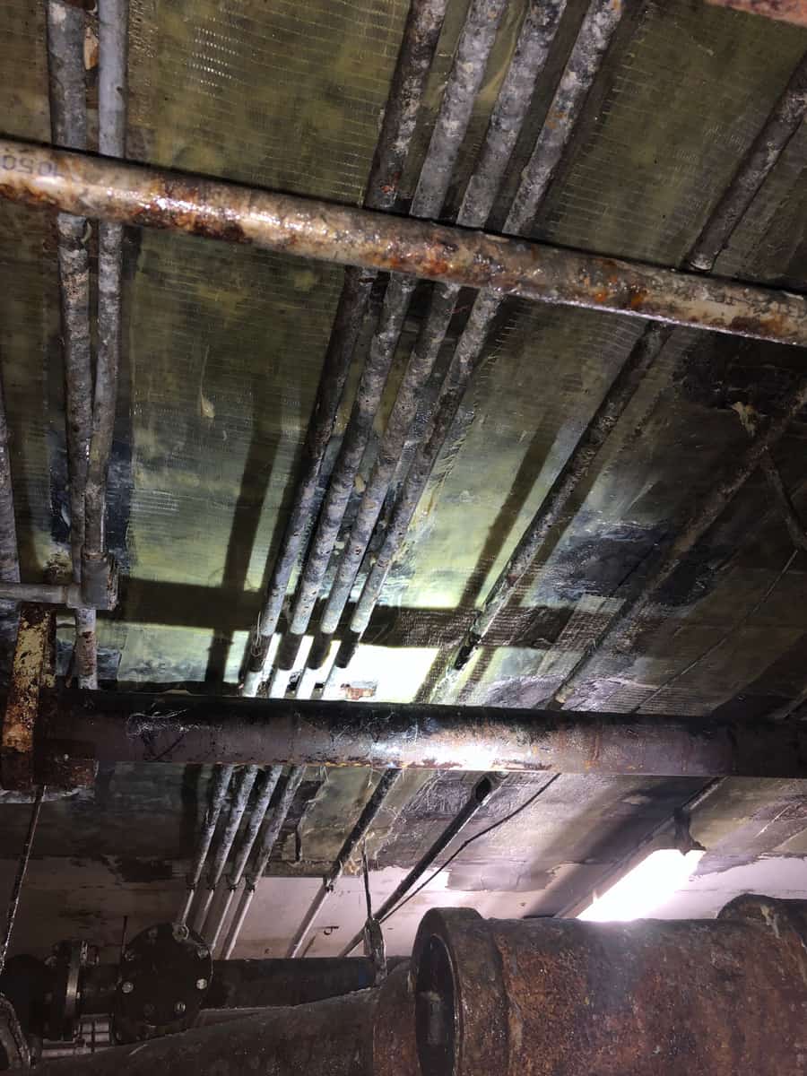 Composite-wrapped slab underside above pipes in a basement.