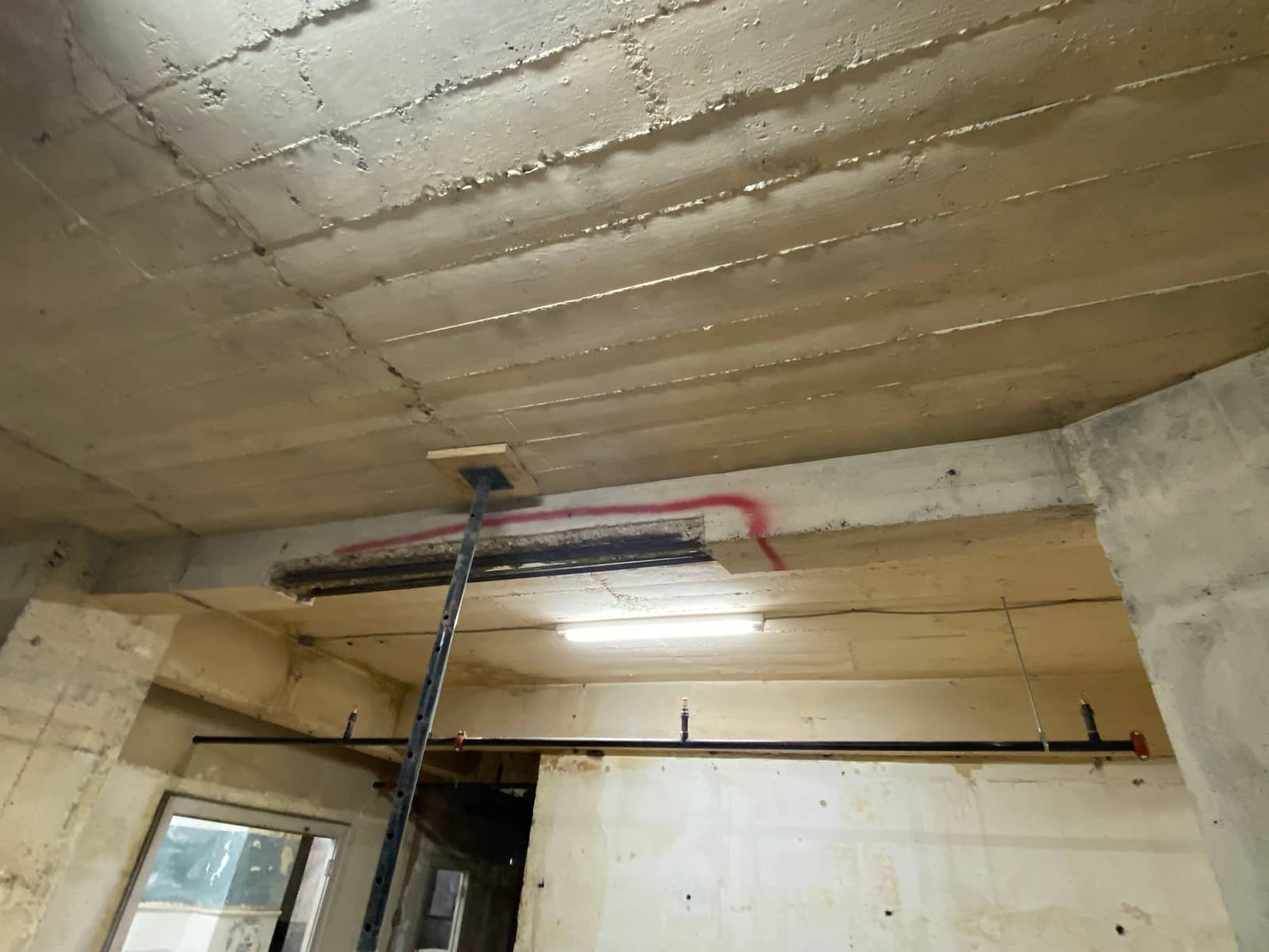 Beam with a red-outlined spall supported by a steel shore post.