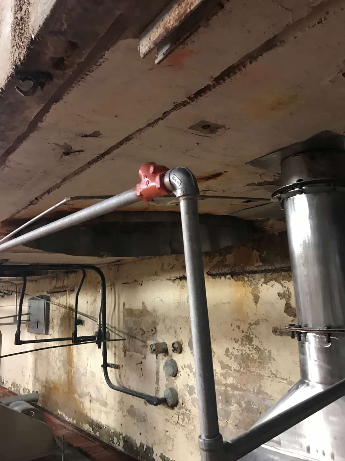 Deteriorated concrete slab and beam underside with stainless pipes and conduit.