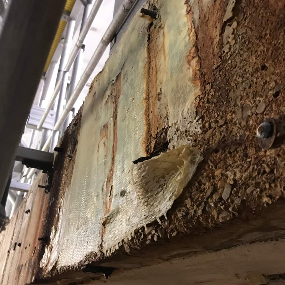 Concrete surface with peeling mesh-reinforced coating and rust staining.
