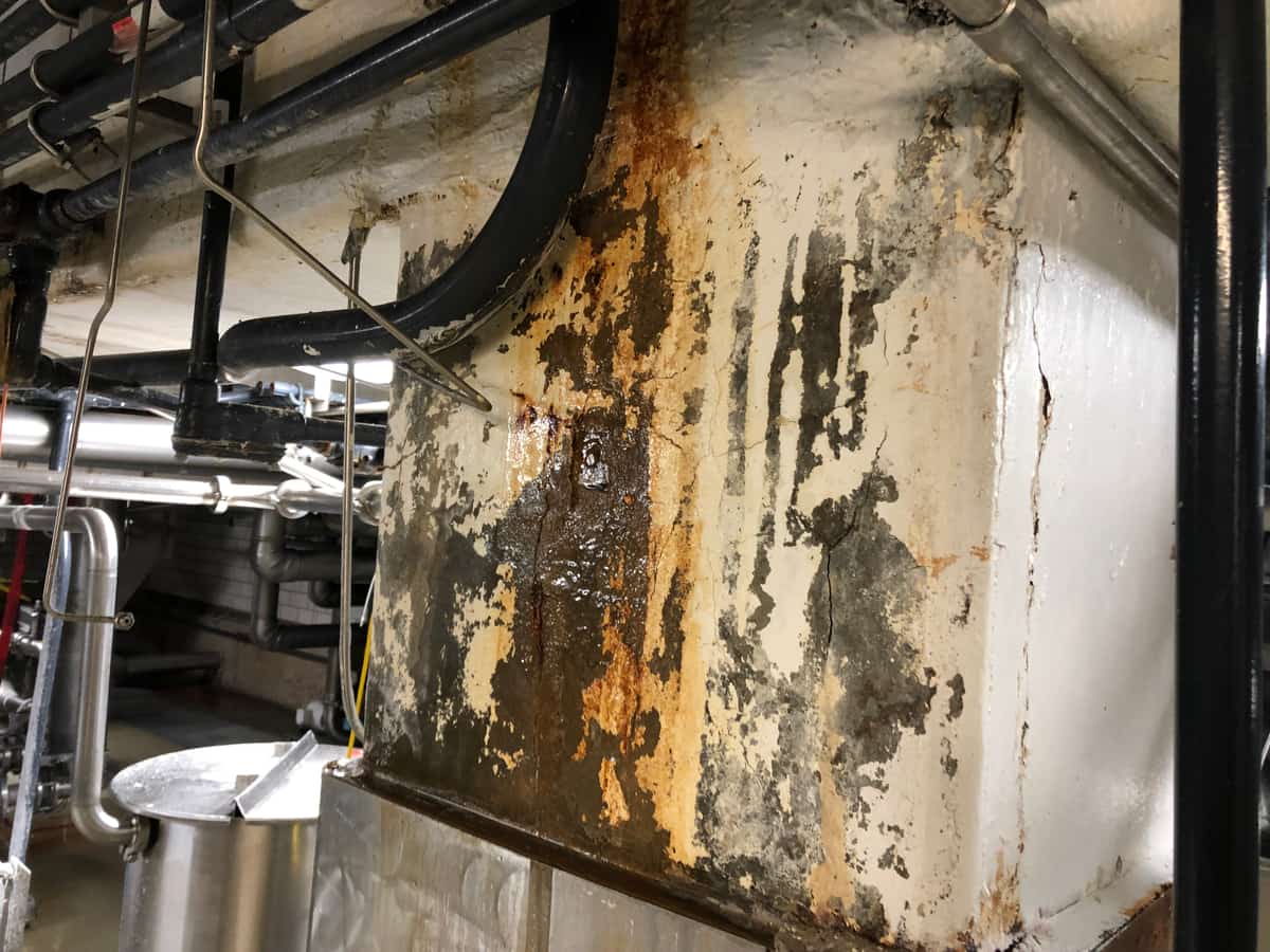 Column heavily stained with rust and peeling paint above stainless base cladding.