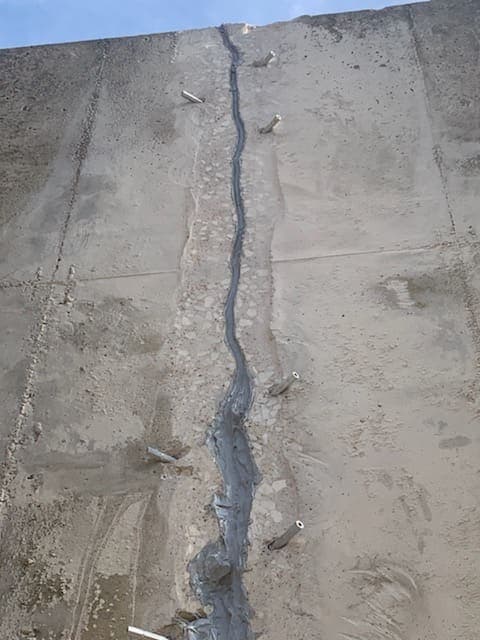 Vertical crack in a concrete wall sealed with gray paste and a line of injection ports.