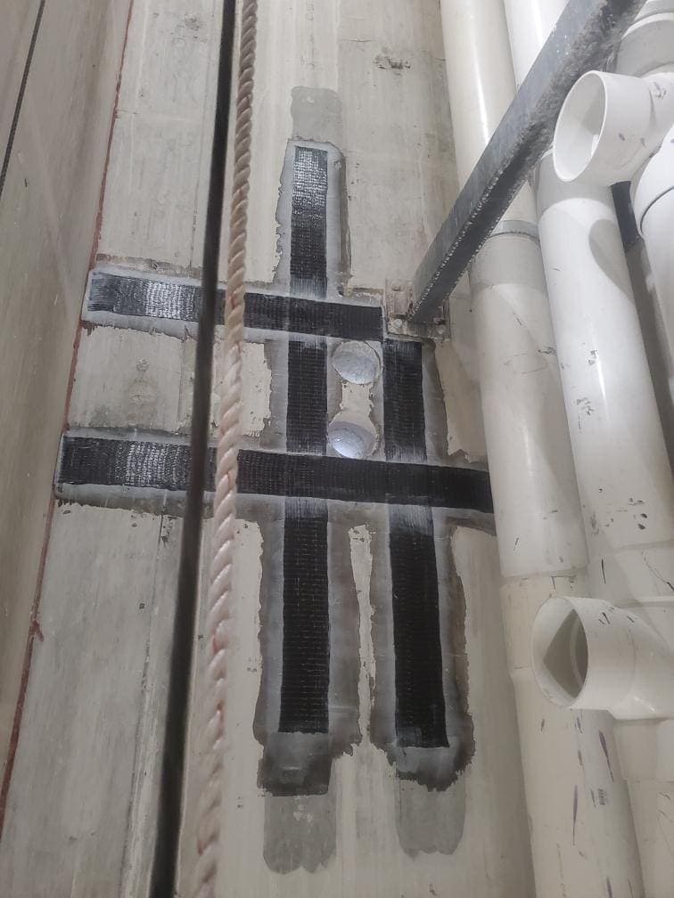 Black composite strips framing penetrations beside PVC pipes in a shaft.