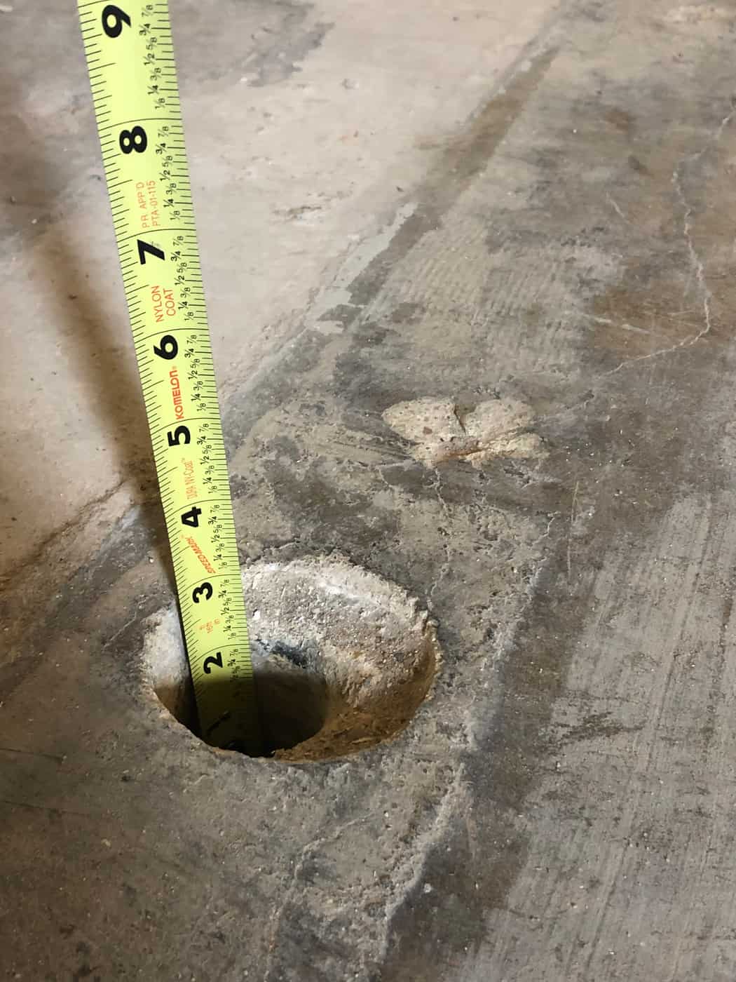 Tape measure set in a core hole through a concrete floor slab.