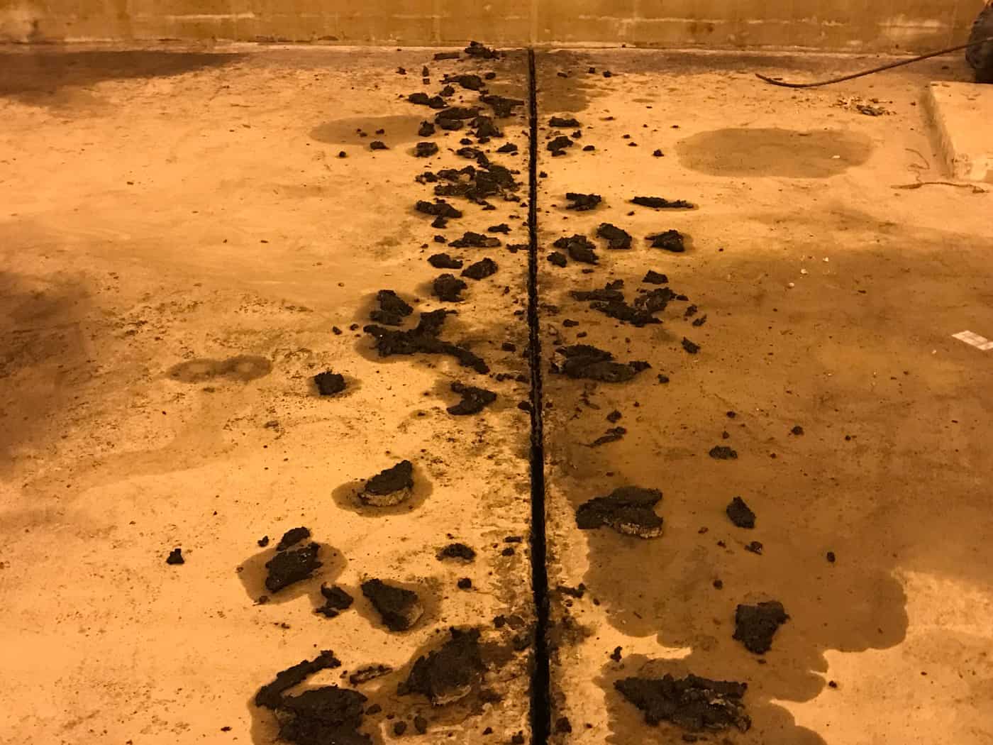 Joint in a concrete tank floor with old sealant removed in dark clumps.