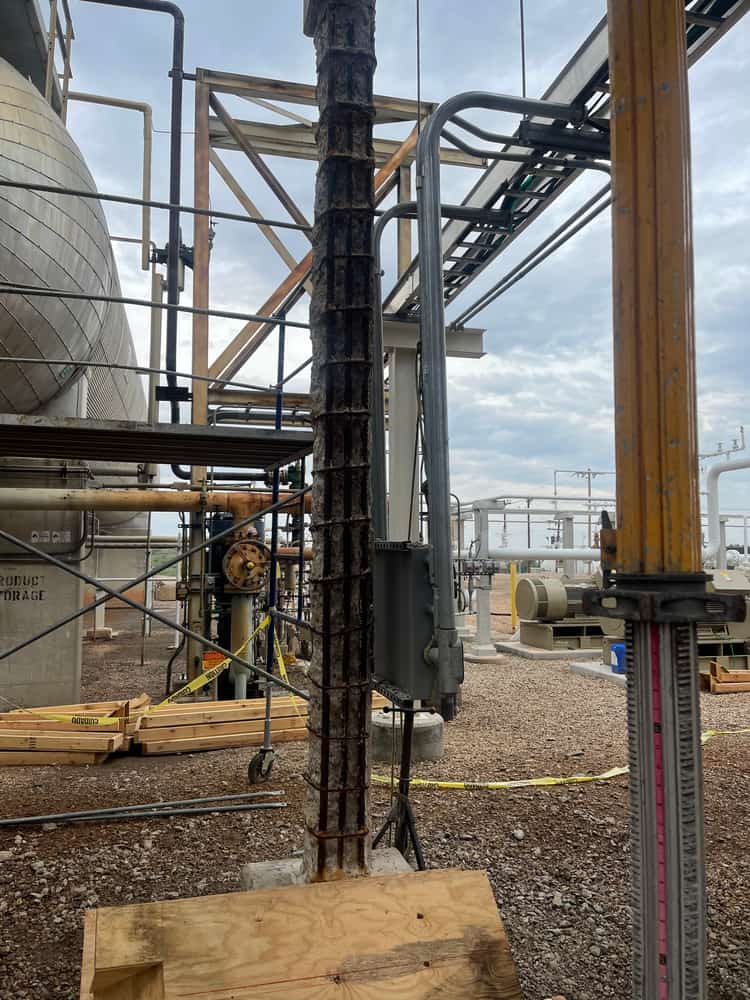 Tall column stripped to its rebar cage beside a steel pipe rack.