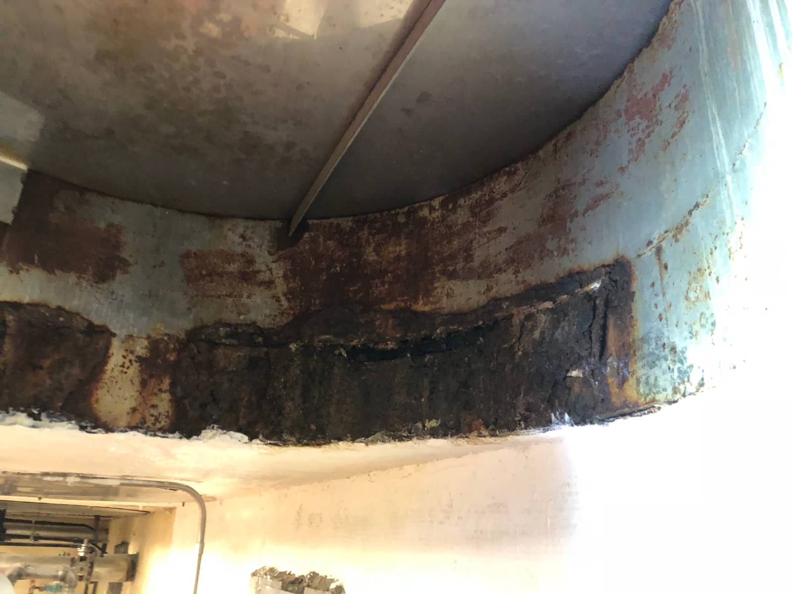 Corroded steel vessel bottom edge resting on a white-coated concrete support.