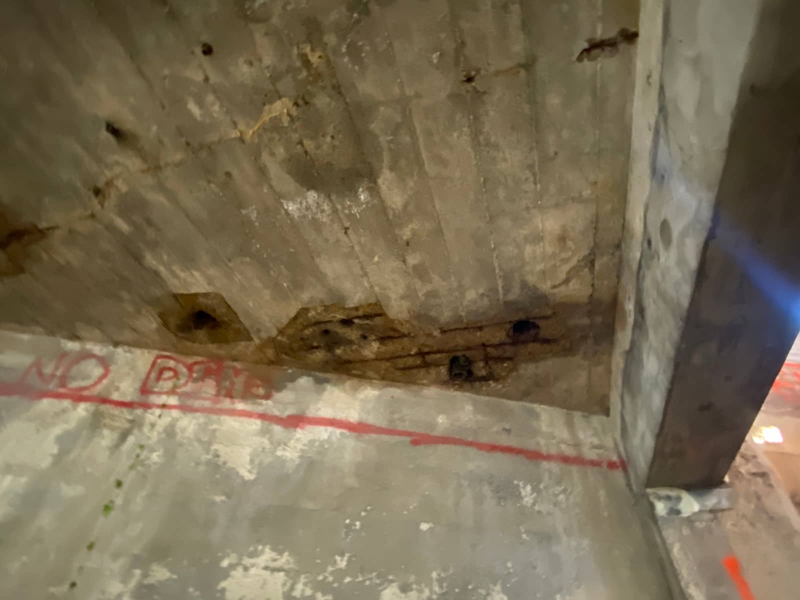 Slab soffit and beam with spalled pockets exposing rebar and a red paint line.