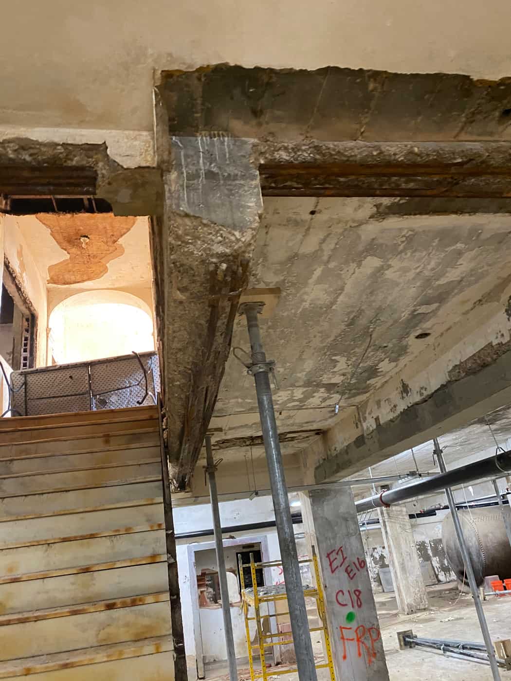 Slab opening above a stair with spalled edges and a steel shore.