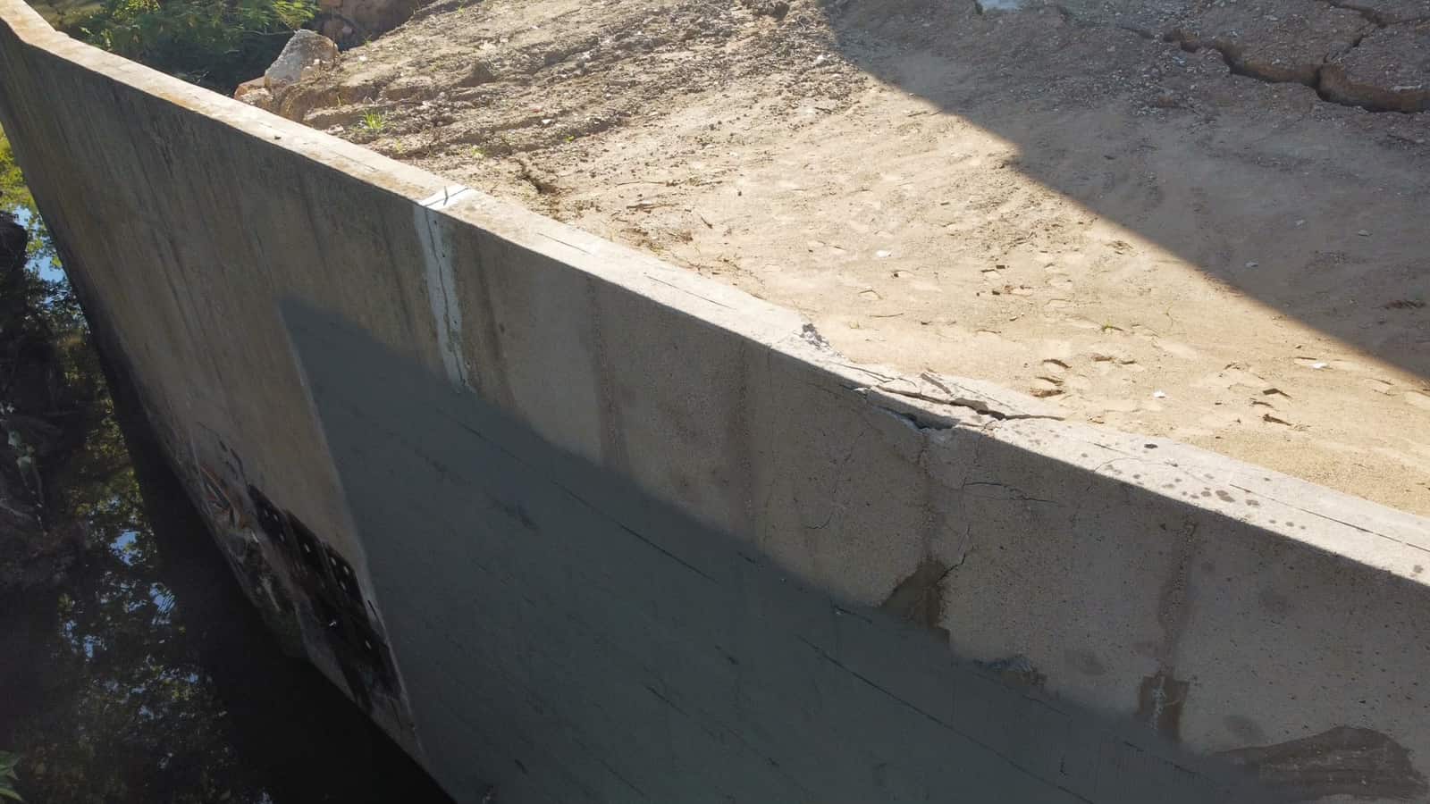 Concrete wall face with a gray coating area and cracked top.