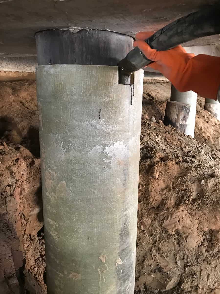 Fiberglass jacket around a round pile being filled at the top beneath a concrete deck.