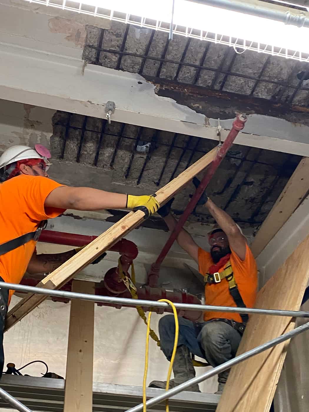 Two workers installing timber shoring under a deteriorated slab.