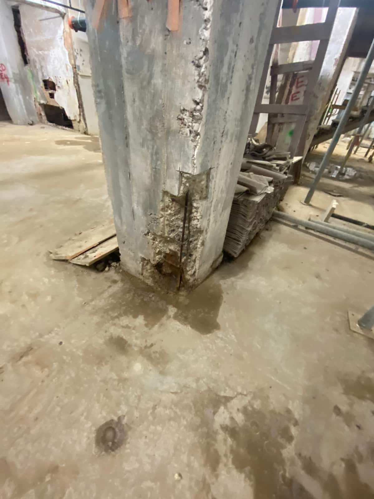 Square concrete column with concrete chipped away at the base corner exposing rebar.