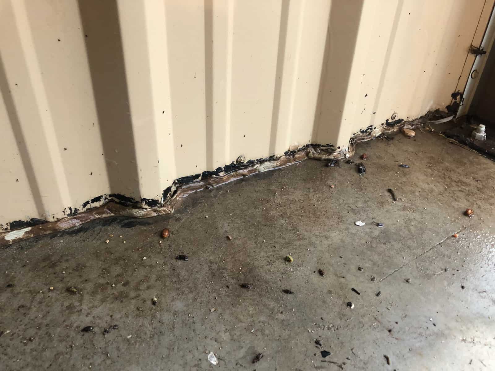 Rusted base of a corrugated metal wall panel where it meets the concrete floor.