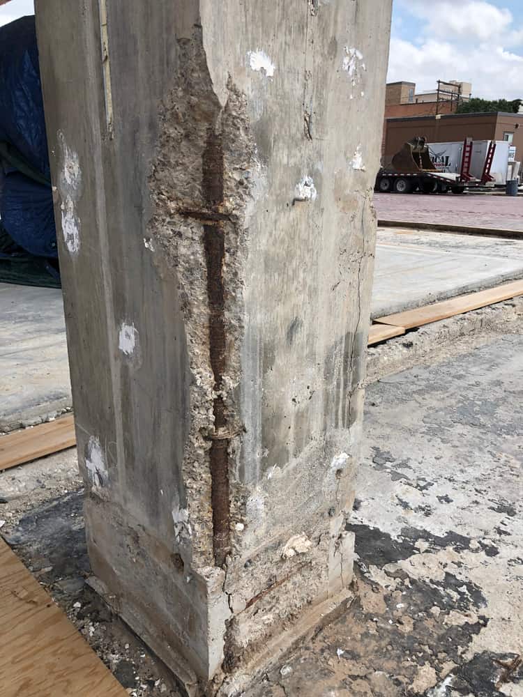 Concrete column with a vertical crack exposing corroded rebar at the corner.