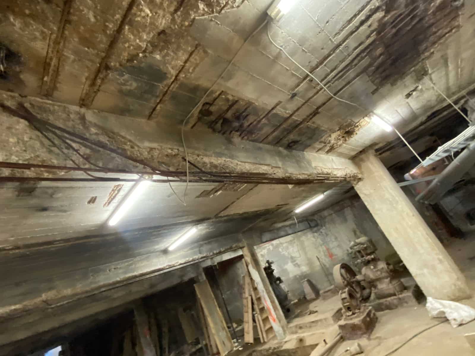Wide basement view of a spalled slab and beams with exposed rebar.