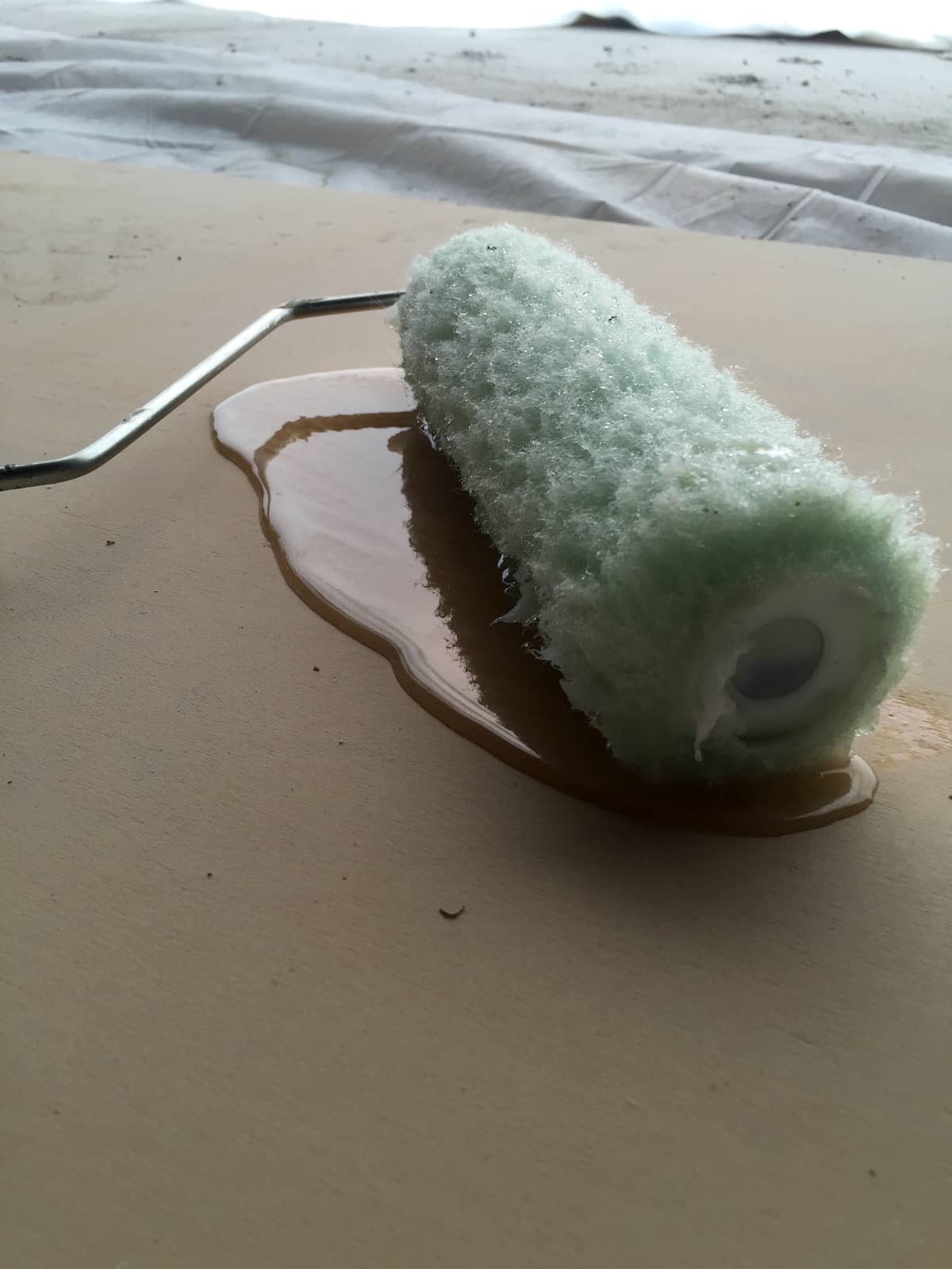 Paint roller resting in a small puddle of resin on a coated surface.