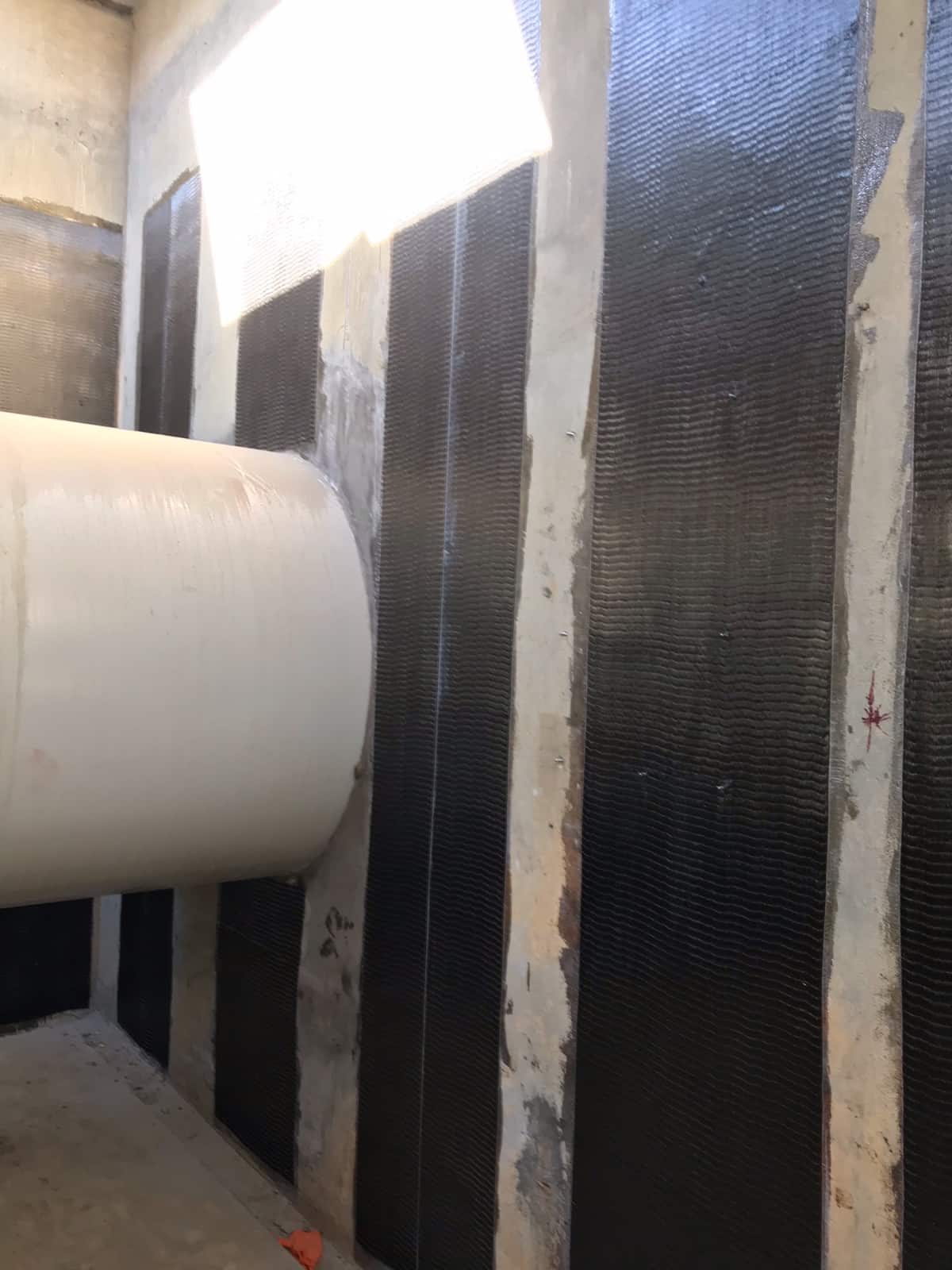 Vertical carbon fiber strips on a concrete wall beside a large white pipe.