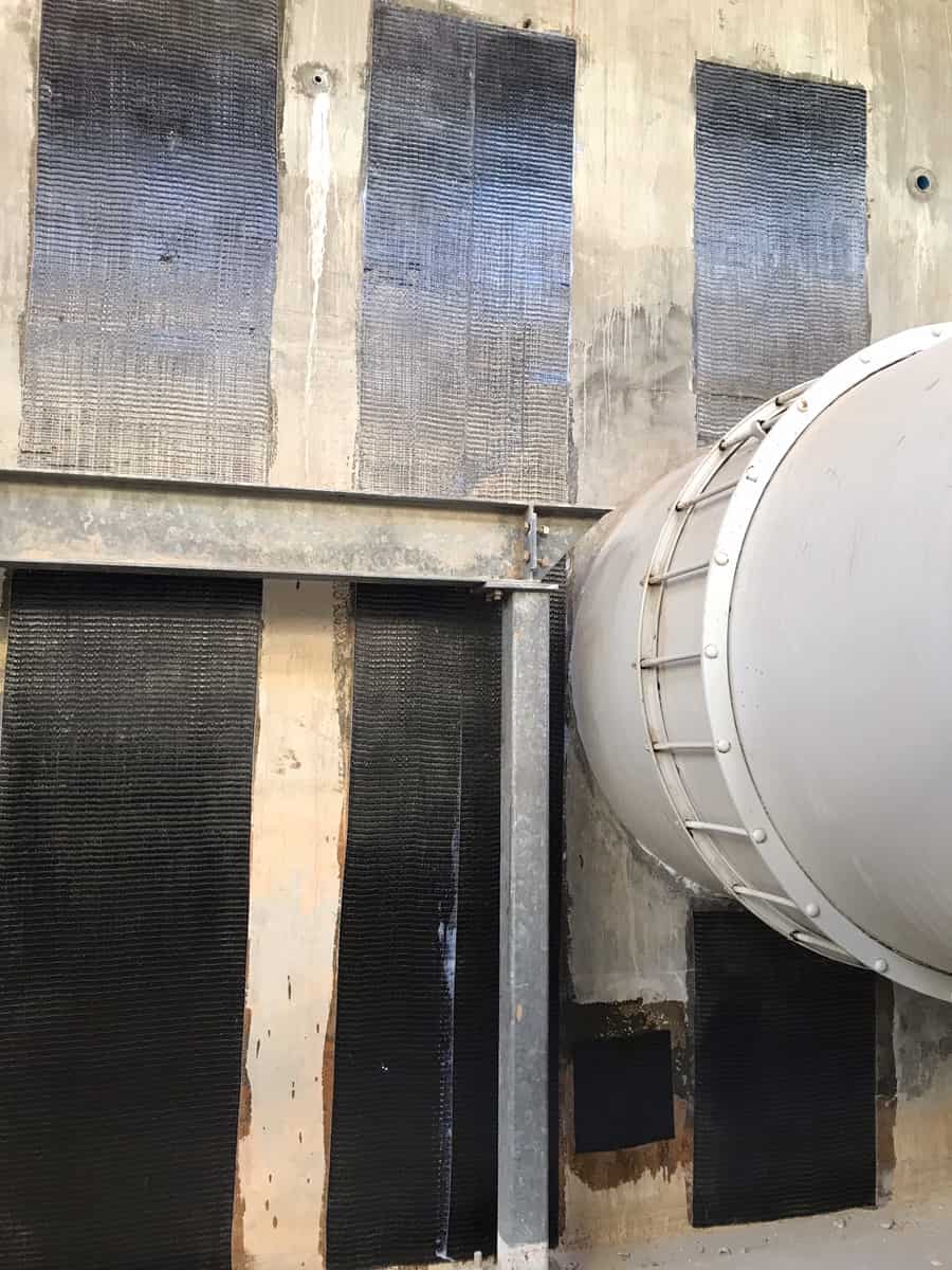 Carbon fiber strips on a concrete wall above and below a steel beam next to a large pipe.