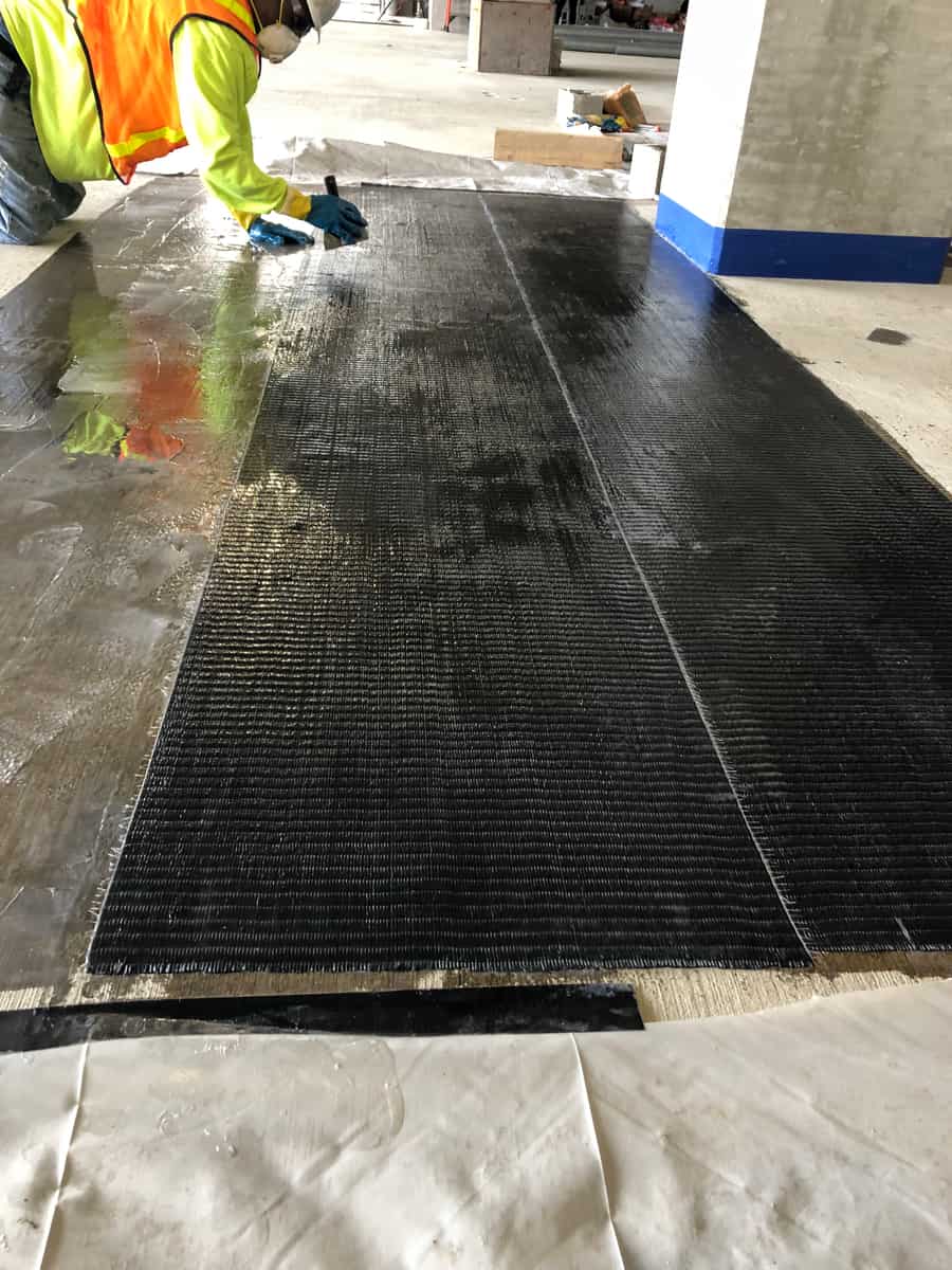 Worker smoothing a saturated carbon fiber sheet on top of a concrete deck.