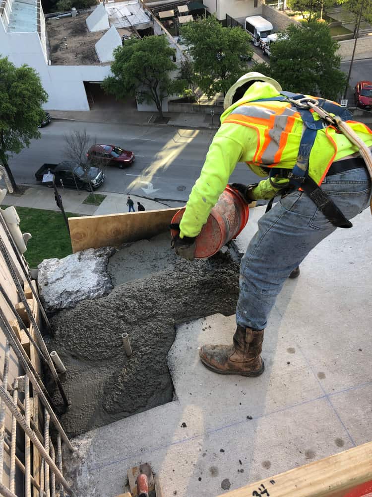 Worker placing concrete at a ledge with rebar high above a street.