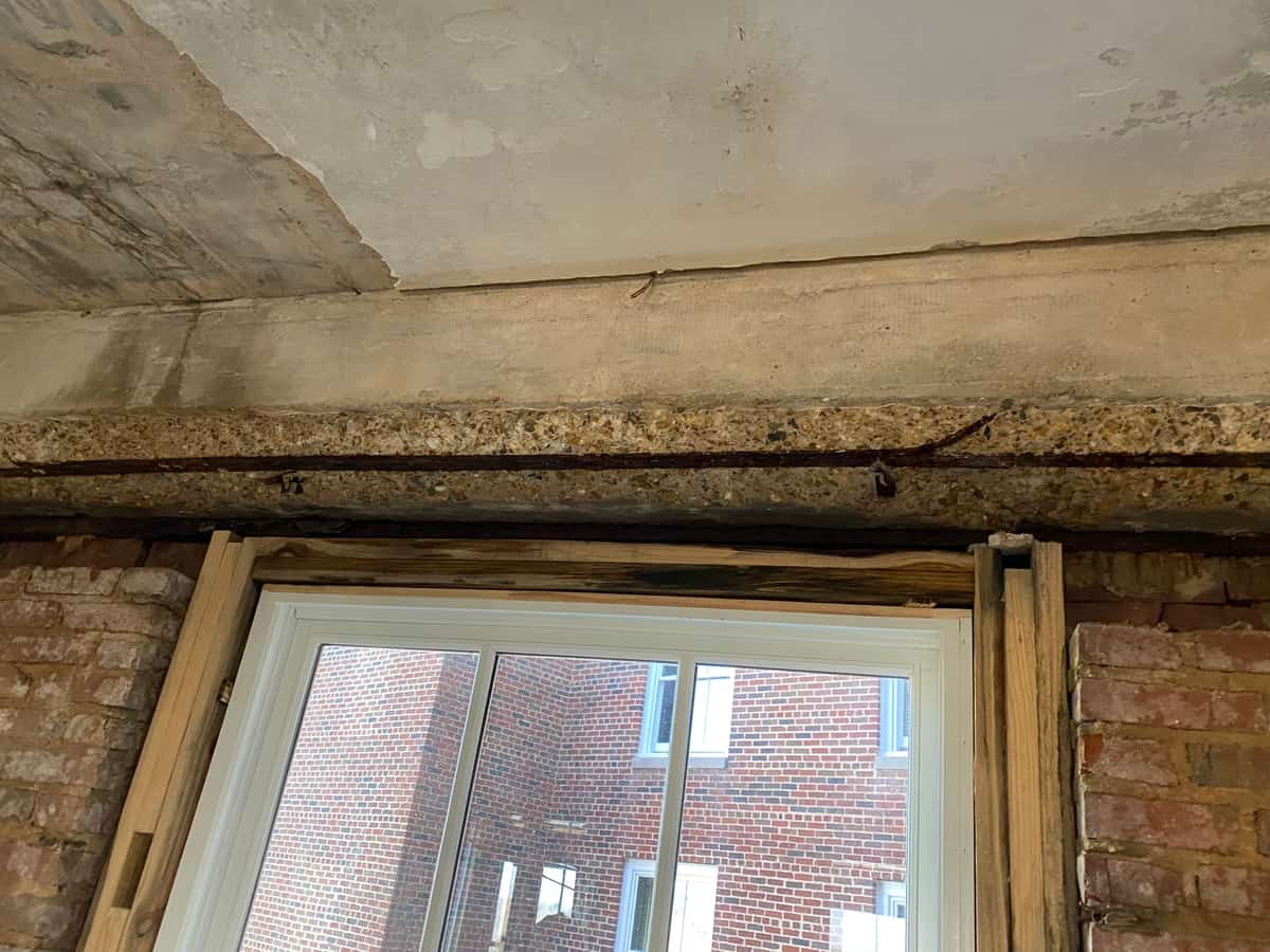 Concrete lintel beam over a window with a spalled soffit and exposed rebar.