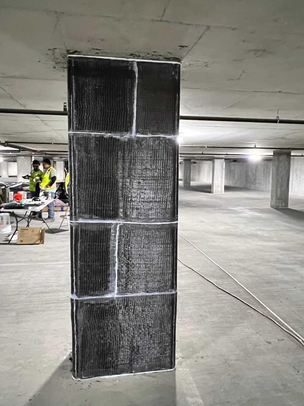 Carbon fiber wrapped column with white seams in a parking garage.