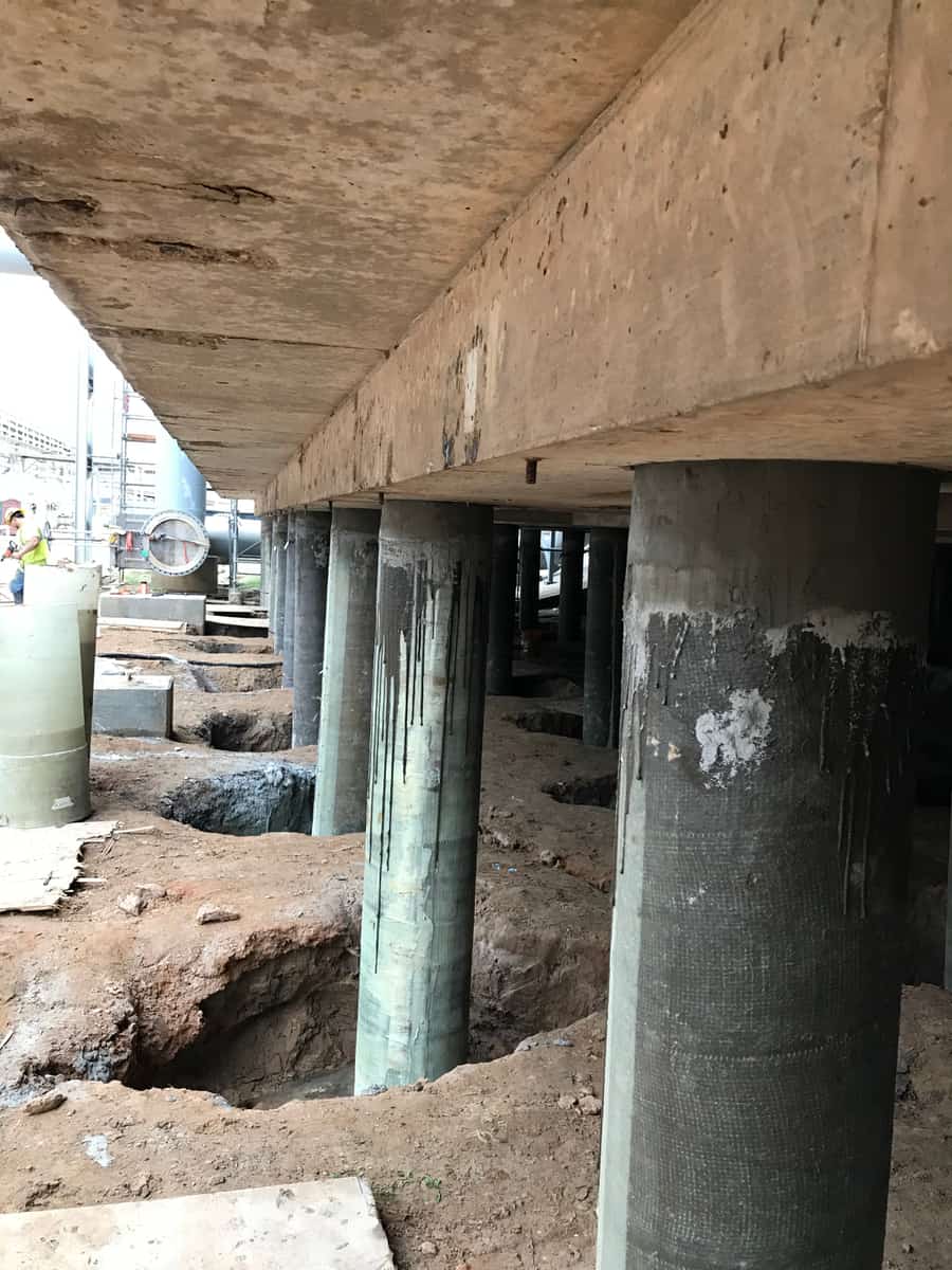 Line of jacketed round piles beneath a concrete deck edge.