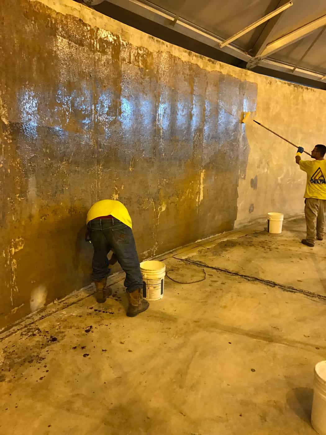 Workers inside a concrete tank rolling saturant onto fabric applied to the wall.