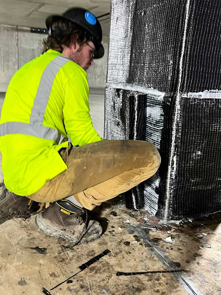 Installer pressing carbon fiber onto the base of a concrete column.