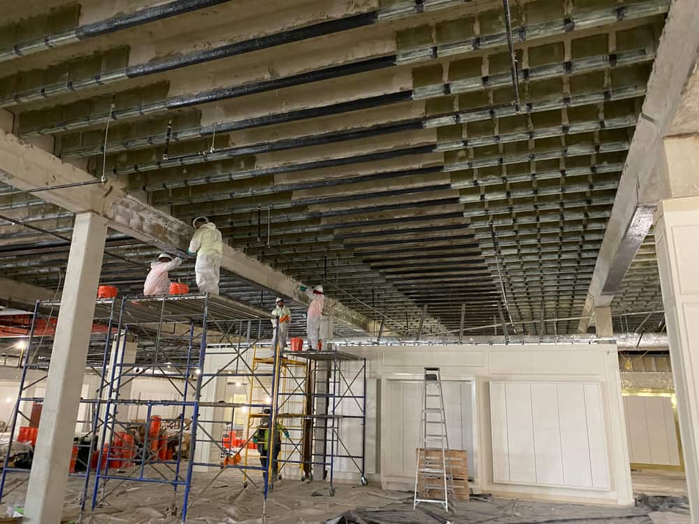 Crew on scaffolding installing carbon fiber strips on the underside of a pan-joist concrete slab.