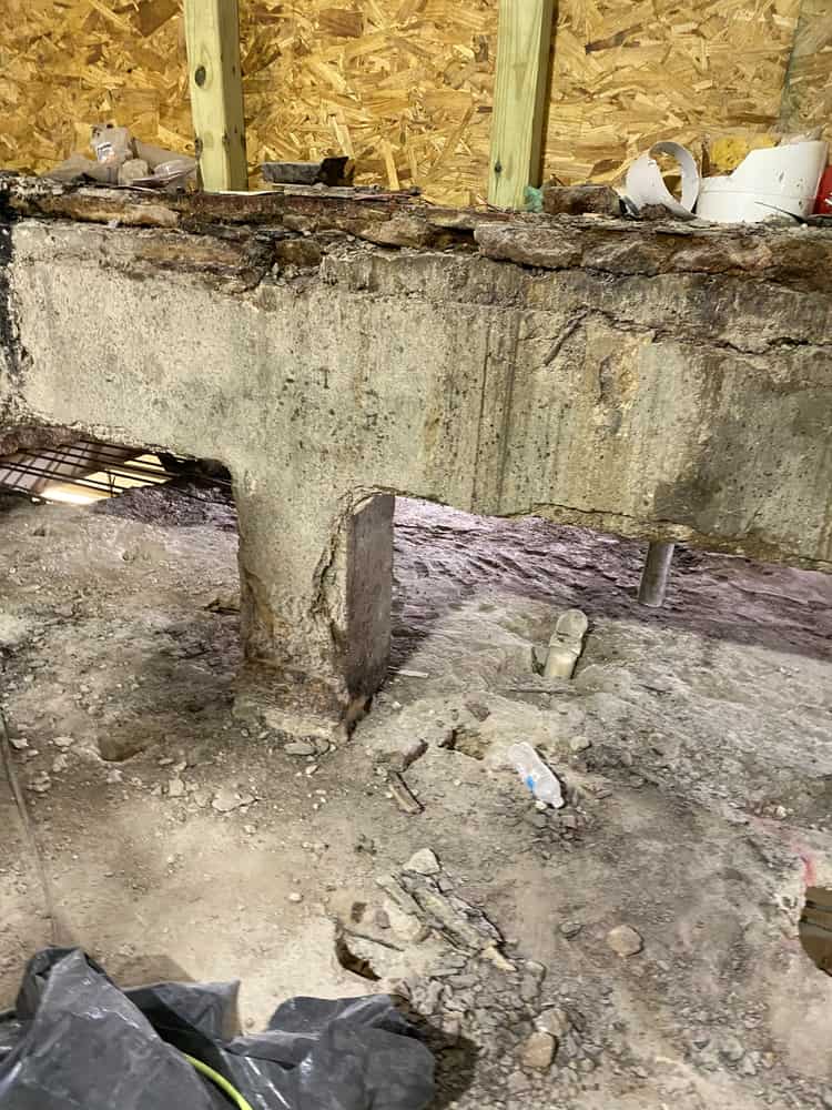 Deteriorated concrete beam on a pier in a crawl space.