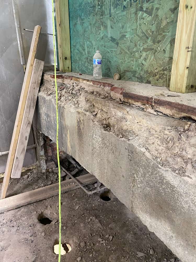 Deteriorated concrete beam with a plumb line in an excavated crawl space.