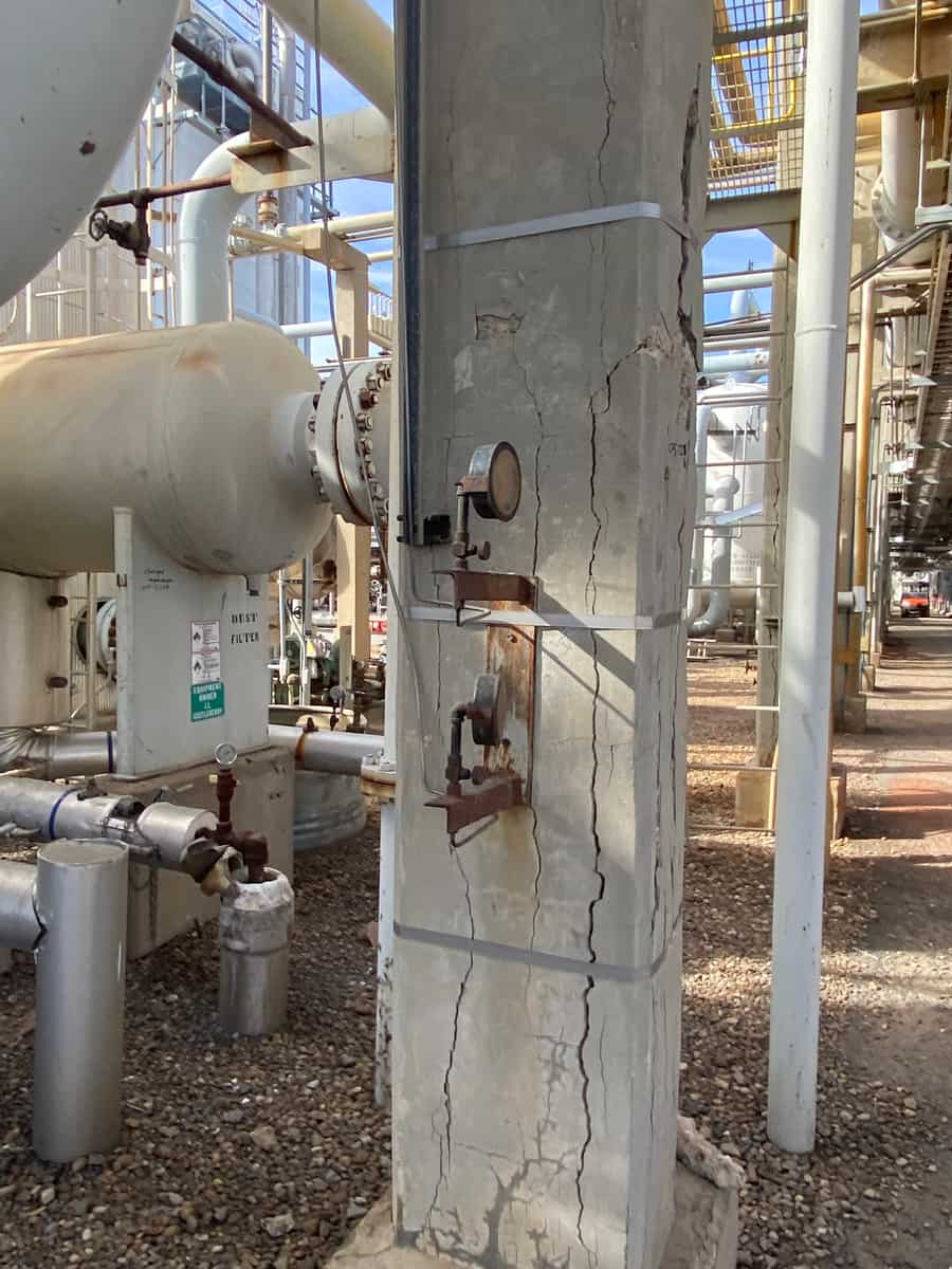 Cracked concrete column with steel bands next to a pressure vessel.