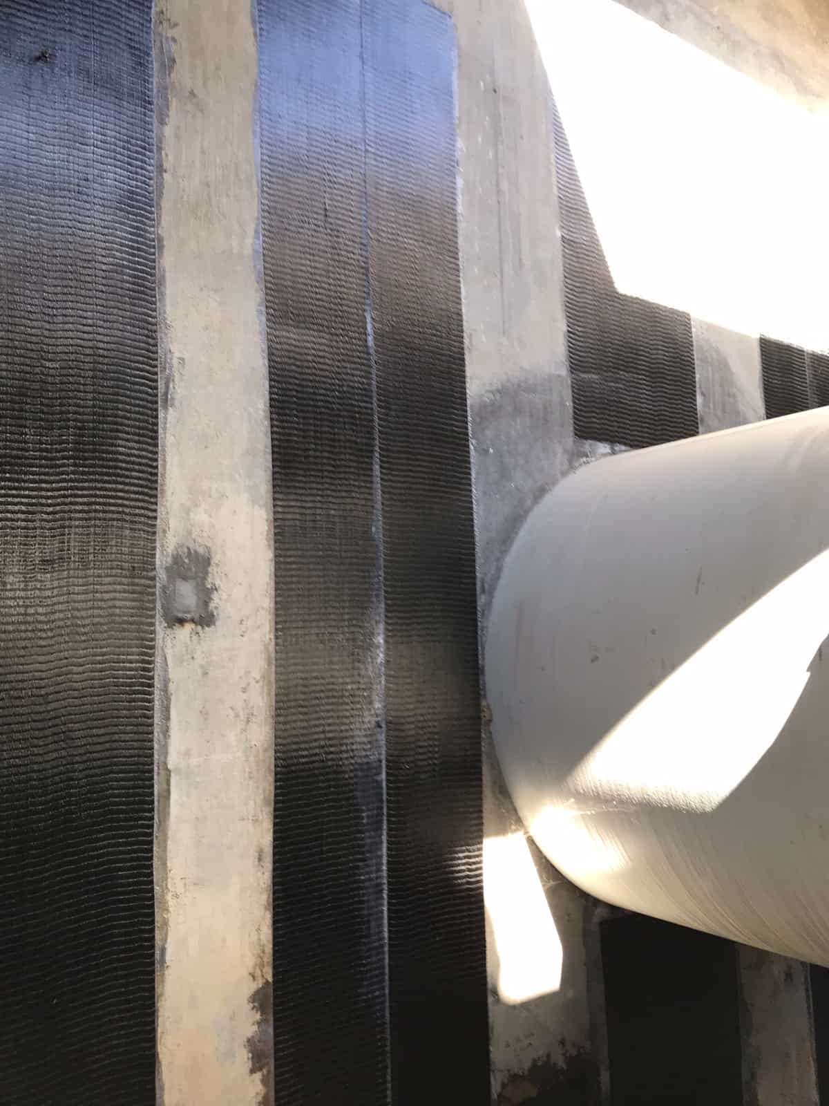 Close view of vertical carbon fiber strips on a wall beside a pipe.