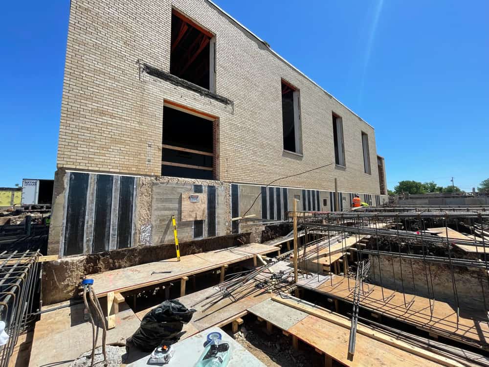 Brick building with vertical black composite strips on the lower foundation wall.