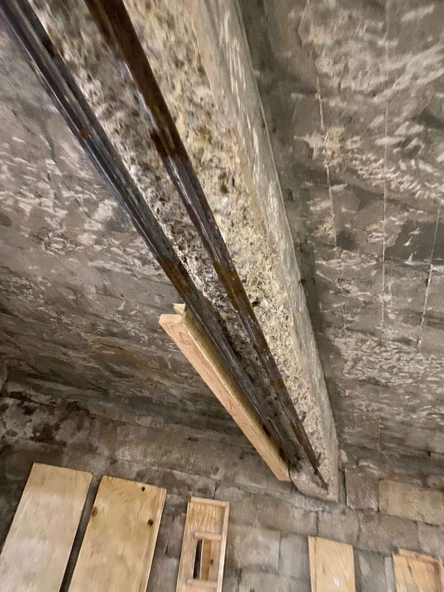 Concrete beam soffit with spalled cover and exposed bars beside a timber brace.