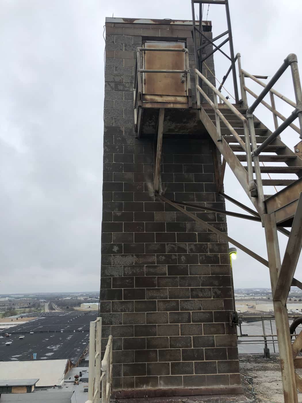 Weathered concrete masonry stair tower with a rusted door and steel access stair.
