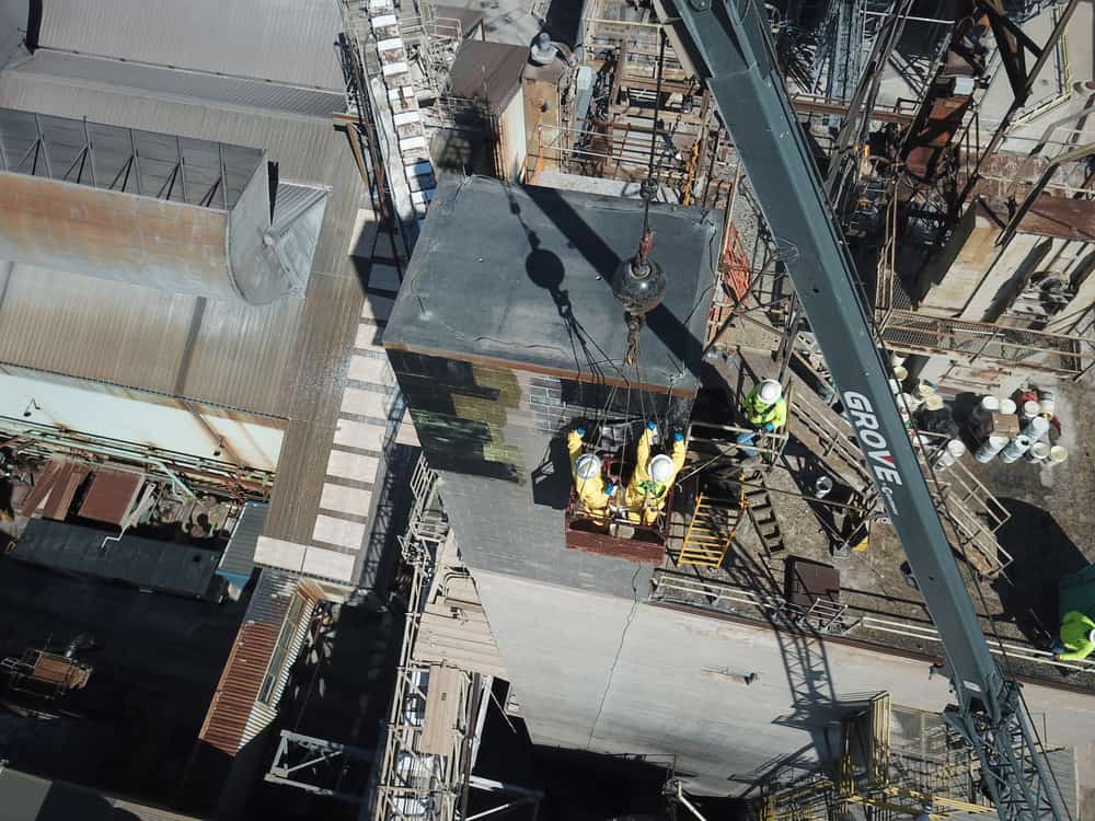 Drone view of workers in a crane-suspended basket at the head house of a concrete masonry tower.