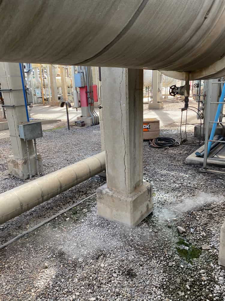 Concrete column supporting a large pipe in a gravel yard.