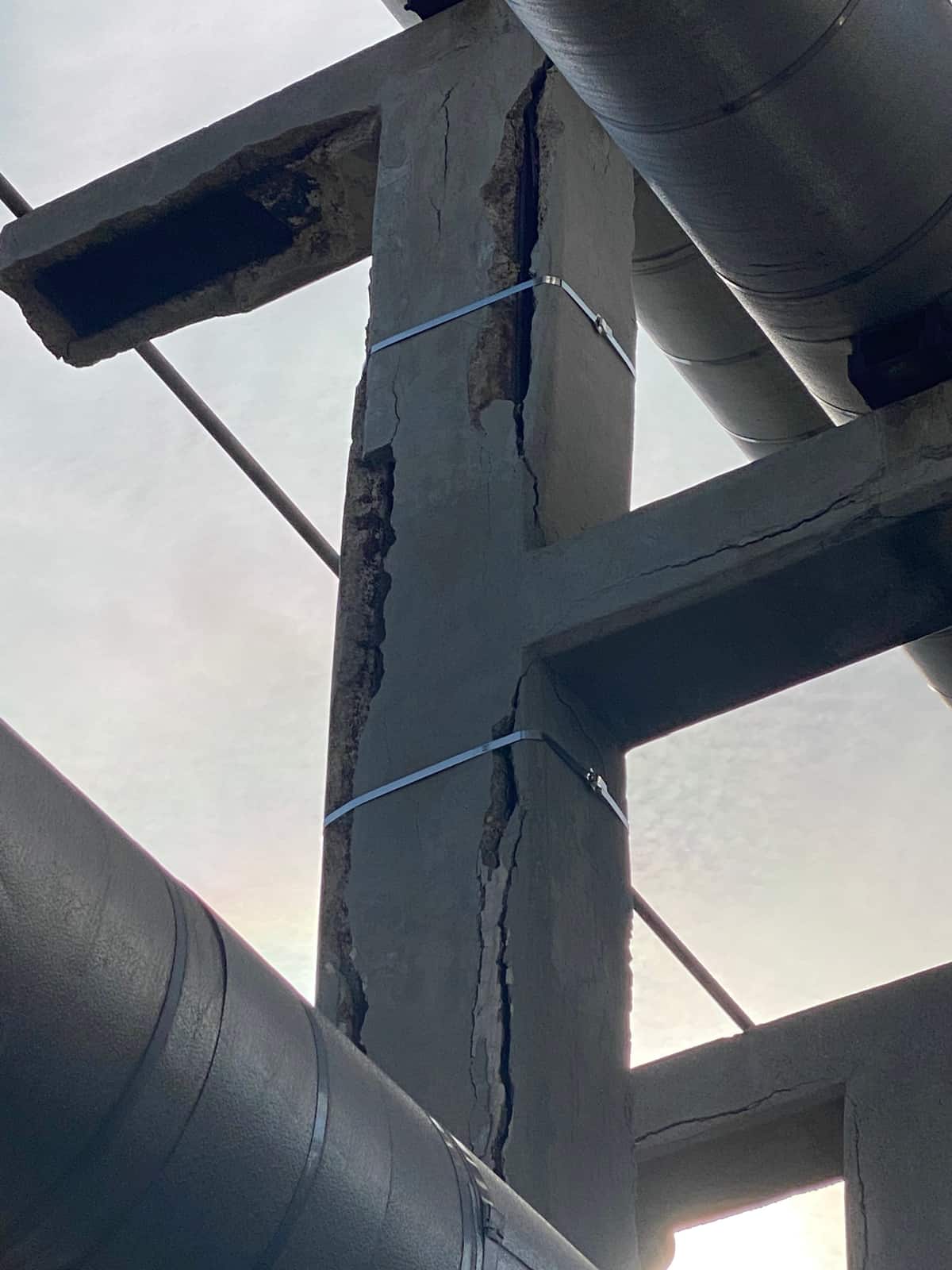 Looking up at a cracked concrete pipe-support frame among pipes.